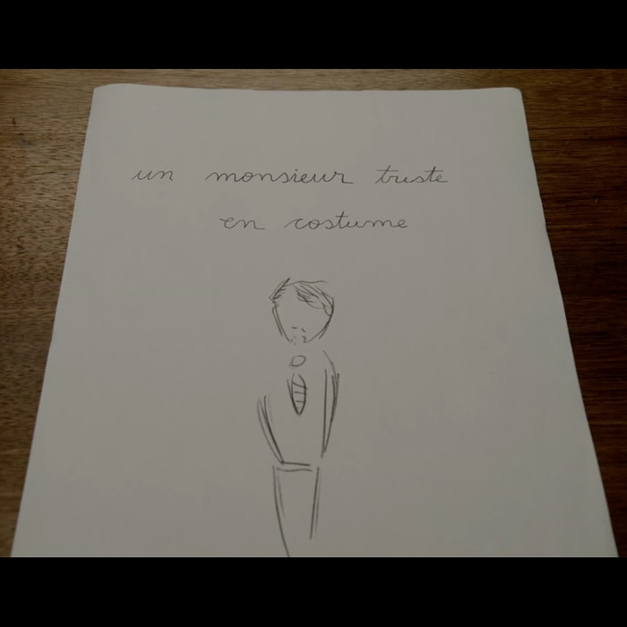 The word's "Un Monsieur Triste En Costume" written in cursive above a sketch of a sad man wearing a suit.